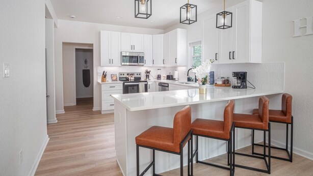 Une cuisine moderne avec des meubles blancs, un îlot central doté de tabourets et des luminaires suspendus.