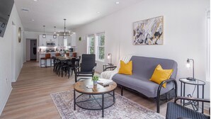 Un salon moderne avec un canapé gris, des coussins jaunes, une table basse ronde et un coin repas comprenant des chaises et une table.