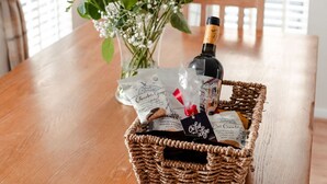 A wooden table with a wicker basket containing a bottle, a gift bag, and a bouquet of flowers. - Lodge 7 by Interhome (Boat of Garten)