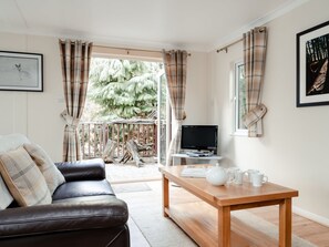 A living room with a leather sofa, a wooden coffee table, a flat-screen TV, and plaid curtains.