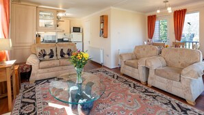 A cozy living room with two sofas, a glass coffee table, and a kitchen area in the background. - Lodge 5 by Interhome (Boat of Garten)