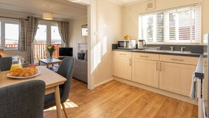 A cozy kitchen with wooden cabinets, a dining area with a table and chairs, and a view of the outdoors through large windows. - Lodge 3 by Interhome (Boat of Garten)