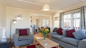 A modern living room with two grey sofas, a wooden coffee table, and a red rug. There is a dining area in the background with a table and chairs. - Lodge 3 by Interhome (Boat of Garten)