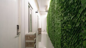 Un couloir avec un mur recouvert de verdure, une porte blanche et un meuble blanc orné de panneaux décoratifs.