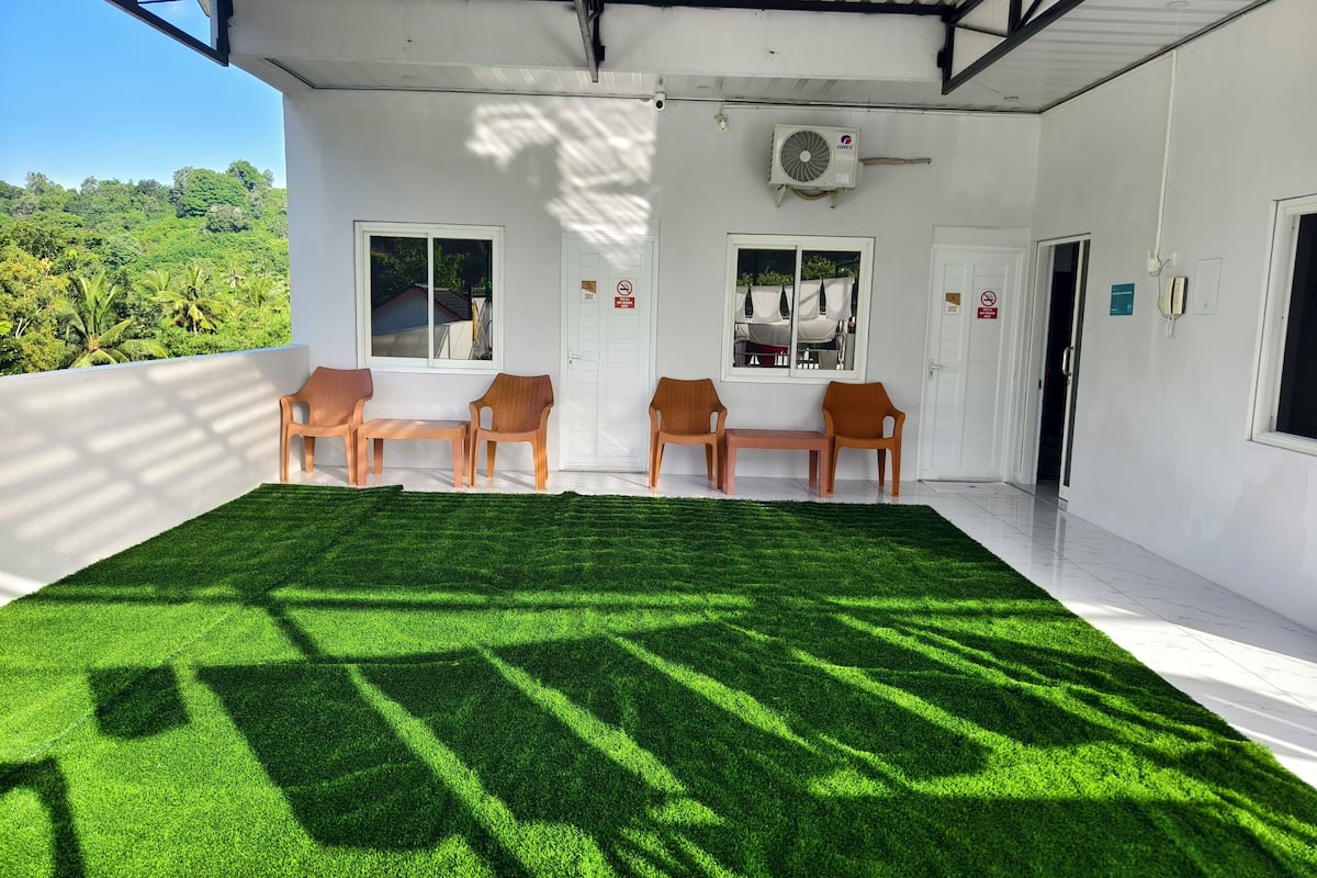 Een kamer met een groot oppervlak van kunstgras, witte muren en een plafondventilator.
