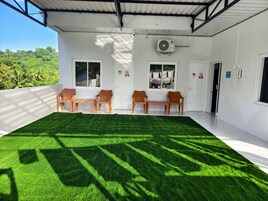 Una habitación con un amplio espacio de césped artificial, paredes blancas y un ventilador de techo.