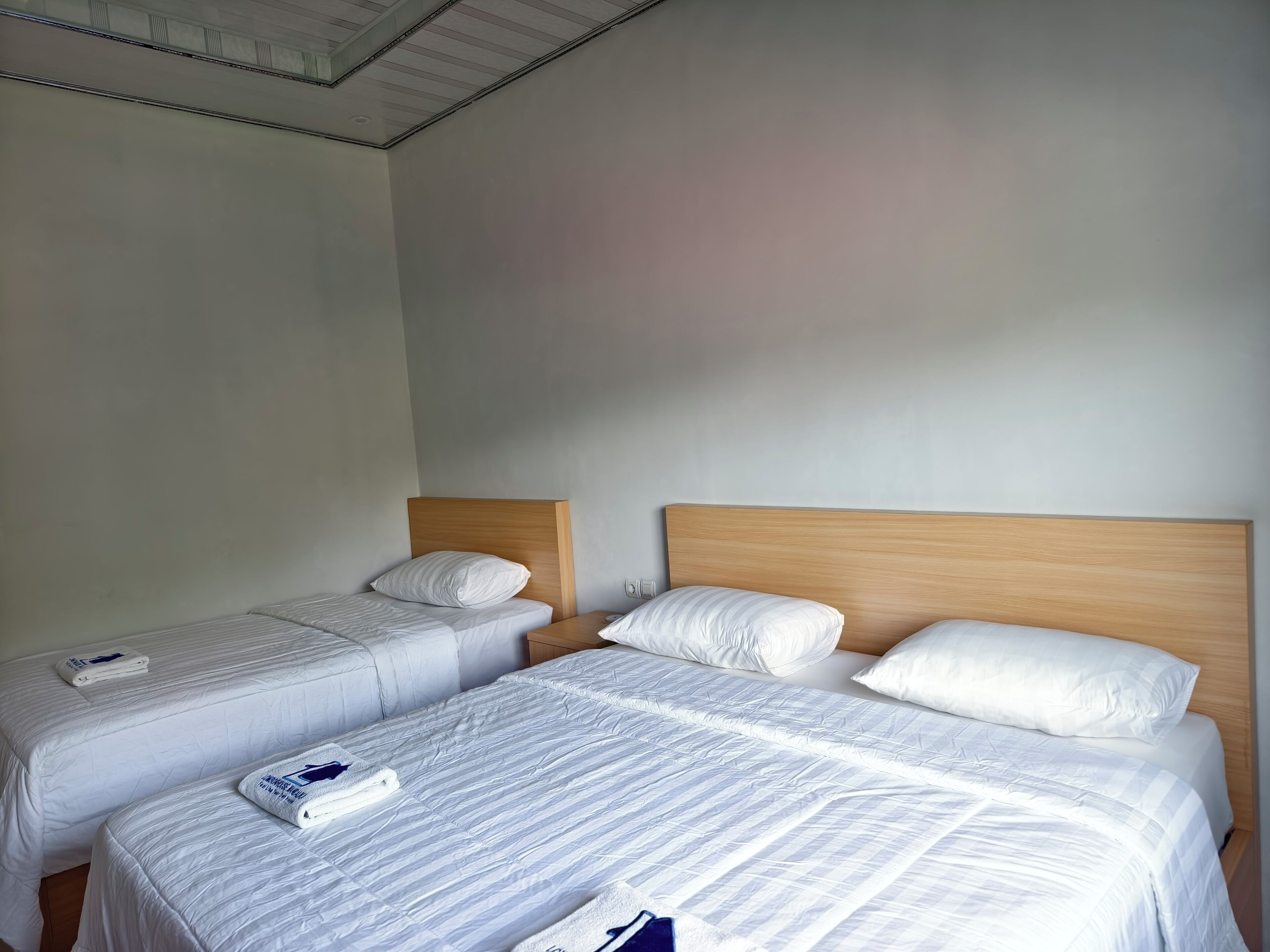 A hotel room with two single beds, each with a wooden headboard and white bedding.