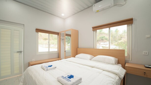 A bedroom with a large bed, two windows, a wooden headboard, a bedside table, and a mirror. - Lombokhouse Mandalika (Kuta)