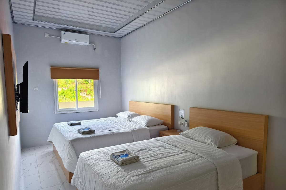 Een kamer met twee bedden, een raam met uitzicht op groen, een plafondventilator en een airconditioning.
