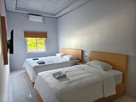 Una habitación con dos camas, una ventana con vistas a zonas verdes, un ventilador de techo y un equipo de aire acondicionado.