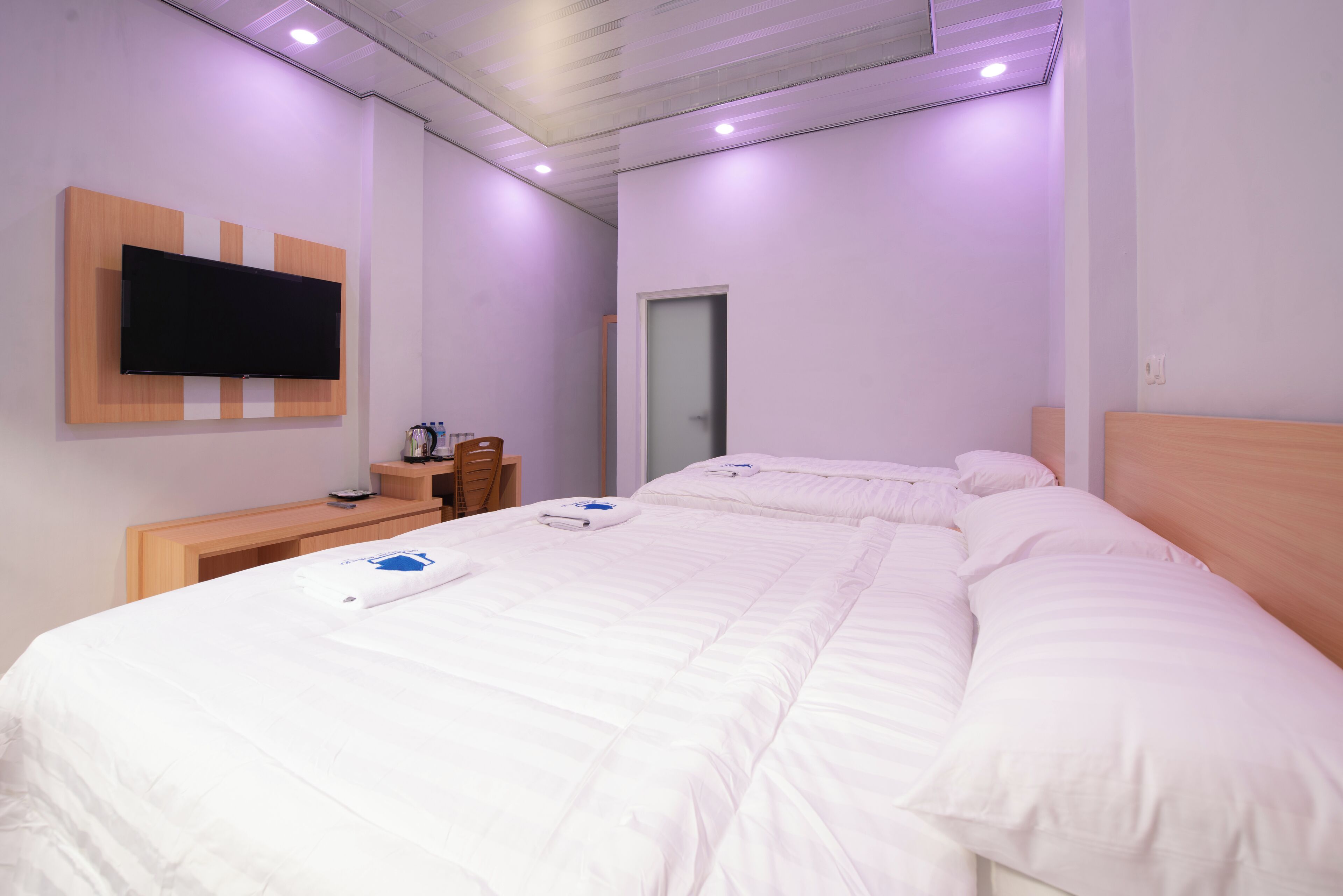 Una habitación de hotel con una cama grande, un televisor de pantalla plana en la pared, un escritorio de madera y una puerta.