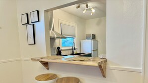 Eine Küche mit Holzarbeitsplatte, zwei Barhocker, einer Pendelleuchte und gerahmten Bildern an der Wand.