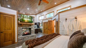 A bedroom with a fireplace, wooden ceiling, and a large bed with a blanket.