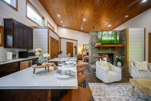 Un amplio salón con chimenea, una mesa de comedor preparada para seis personas y una cocina con armarios de madera oscura y una isla grande.