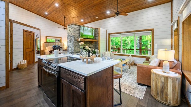 A spacious kitchen with a central island, a dining area with a sofa, and a large window offering a view of the outdoors.