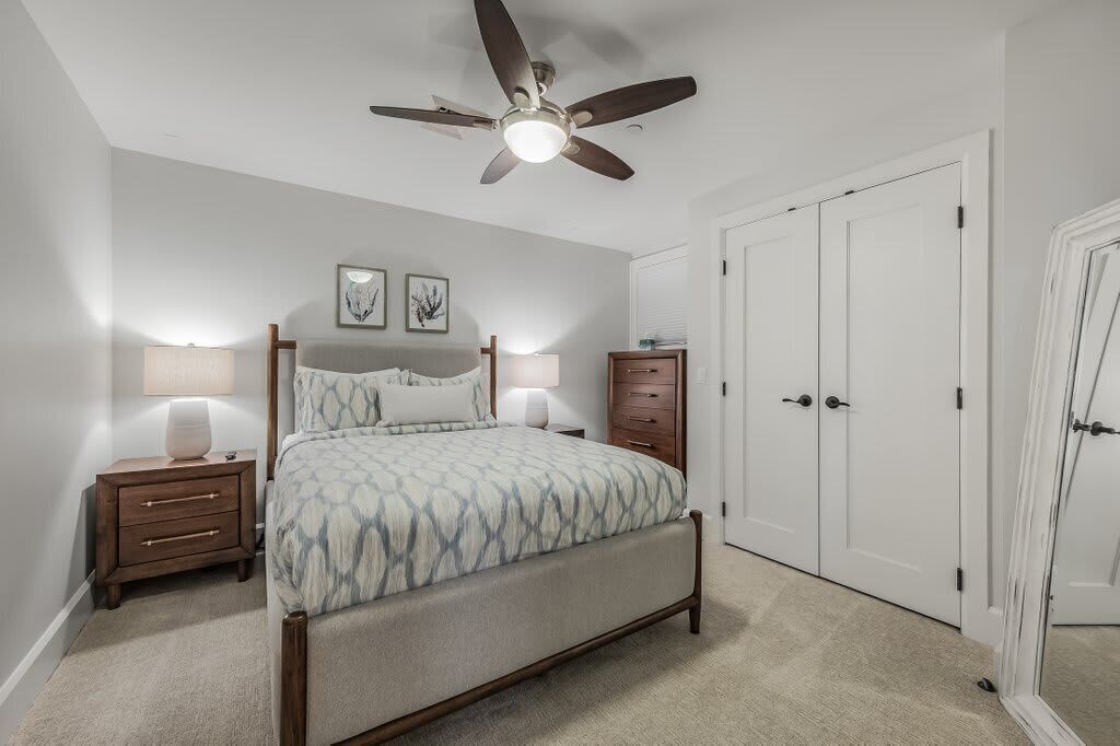 A bedroom with a bed, bedside lamps, a ceiling fan, a wardrobe, and a door.