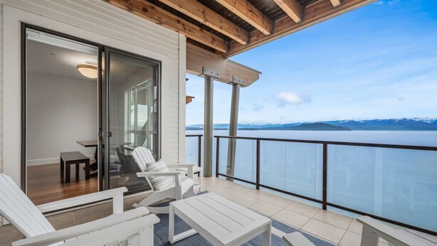 Un balcon avec vue sur un lac et des montagnes, des meubles blancs et un plafond en bois.
