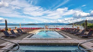 Un espace piscine avec des chaises longues et une vue sur un plan d’eau et des montagnes.