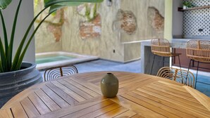 Taula de fusta amb un ram, cadires de vímet, una planta en test i vista a una piscina i mur exterior.