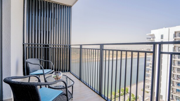 A balcony with two wicker chairs and a small table, overlooking a body of water and buildings. - Maison Privee - Modern Yas Island Escape w/ Peaceful Canal Views (Abu Dhabi)