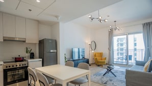 A modern kitchen with a stove, refrigerator, and dining area. There is a sofa and a balcony with a view of buildings. - Maison Privee - Modern Yas Island Escape w/ Peaceful Canal Views (Abu Dhabi)