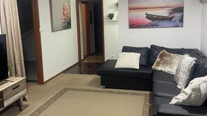 Una sala de estar con un sofá negro, un televisor, un ventilador de techo y un cuadro de un barco en el agua.