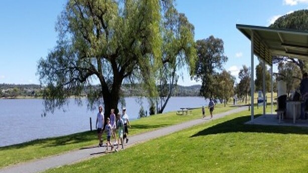 Un parque con un sendero, zona de picnic y un lago.