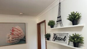 Un pasillo con una obra enmarcada de flores rosadas, un letrero que dice "SIMPLY Blessed" y tres plantas en macetas sobre estantes blancos.