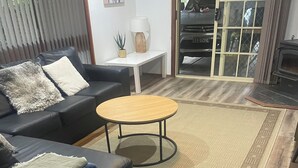 Una sala de estar con un sofá de cuero oscuro, una mesa redonda de madera y una alfombra estampada.
