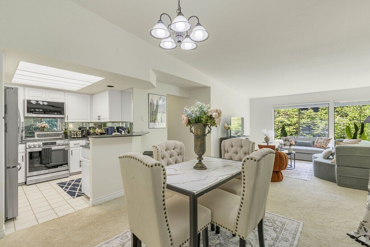 A modern kitchen with white cabinets, a dining area with a marble table, and a living room with a gray sofa.