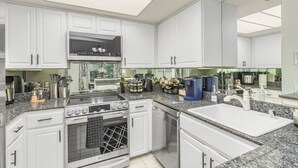 Eine moderne Küche mit weißen Schränken, einem eingebauten Backofen, einem Gasherd und einer großen Kücheninsel mit Spüle.