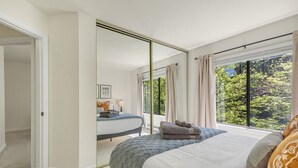 Ein Schlafzimmer mit einem großen Bett, einem Spiegel und Blick auf Grünflächen.