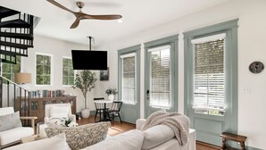 A spacious living room with a sofa, a dining area with a table and chairs, a staircase, and large windows with shutters. - "Idlehour" new cottage in Fairhope, AL - NEW LISTING (Fairhope)