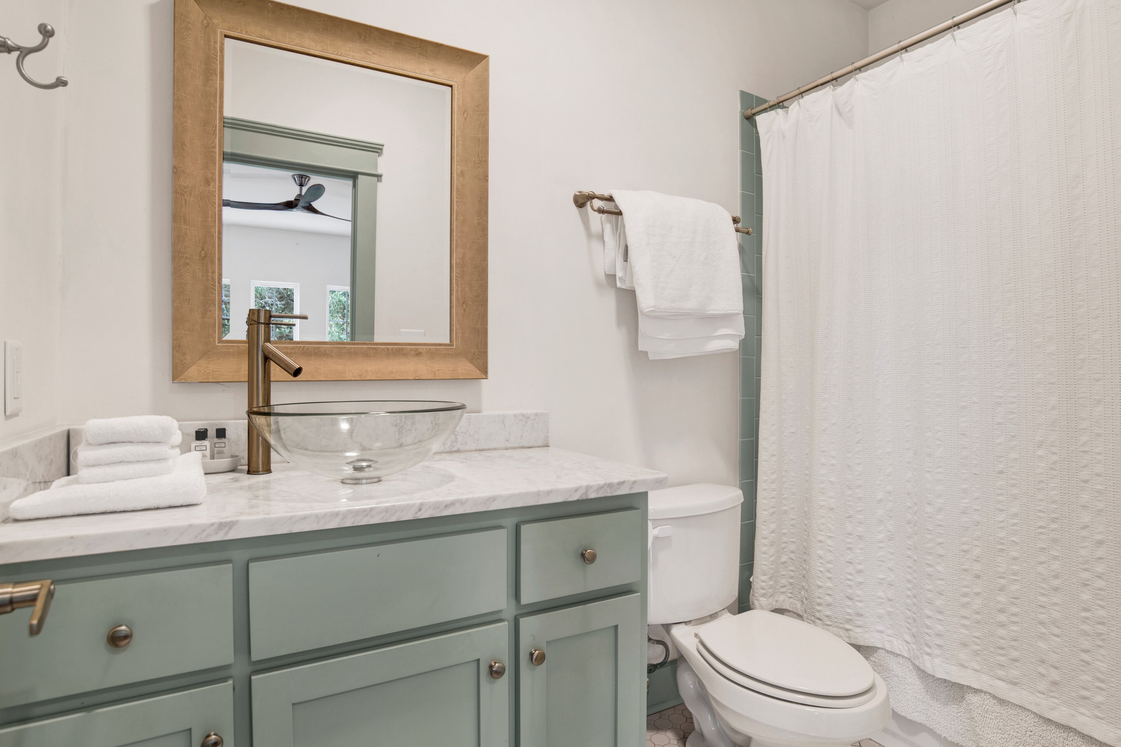 Un bagno con un lavabo in marmo, una ciotola in vetro, uno specchio con cornice in legno, un water e una tenda per la doccia.