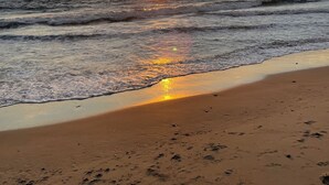 Une plage avec des vagues, un coucher de soleil et un ciel dégagé.