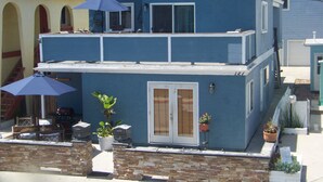 Une maison à deux étages dotée d’un balcon, d’un espace salon extérieur et de plantes en pot.