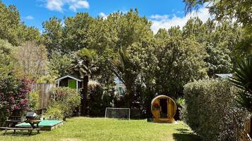 Enjoy a serene natural setting surrounded by lush trees and shrubs, with a rustic wooden barrel and a charming outdoor structure.
