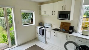 Una cocina compacta con armarios blancos, estufa, fregadero, microondas y lavadora.