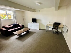 Cozy living space with a sofa, coffee table, flat-screen TV, desk, and large window.