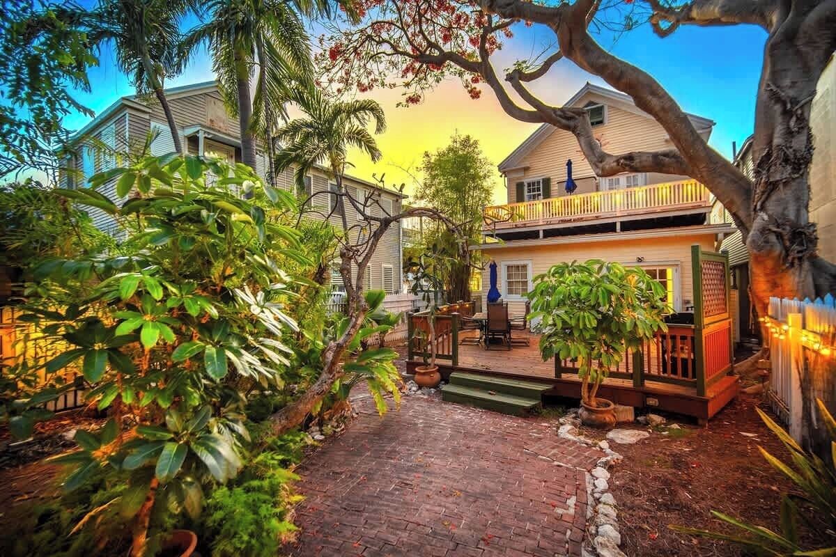 A house with a porch, surrounded by lush greenery and a brick pathway.