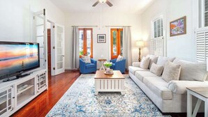 A living room with a TV, blue chairs, a white sofa, a wooden coffee table, and a ceiling fan. - Key Lime Hideaway (Key West)