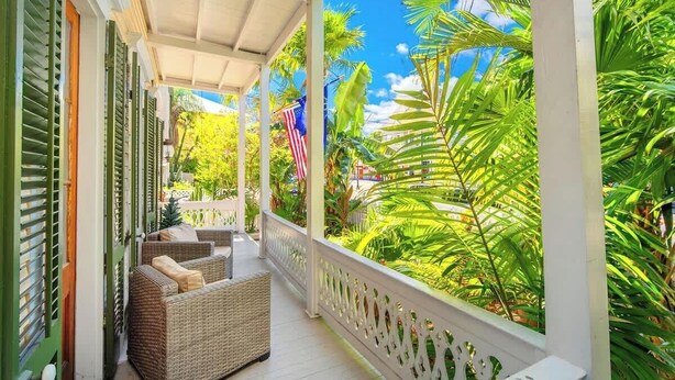 A covered porch with wicker furniture and a view of lush greenery and a clear blue sky. - Key Lime Hideaway (Key West)