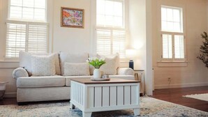 A living room with a beige sofa, a white coffee table with a vase of flowers, and a painting on the wall. - Key Lime Hideaway (Key West)