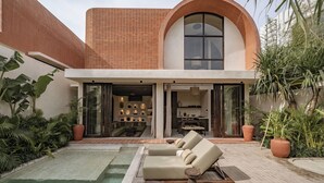 A modern house with a swimming pool, a lounge area with two sunbeds, and a large arched window.