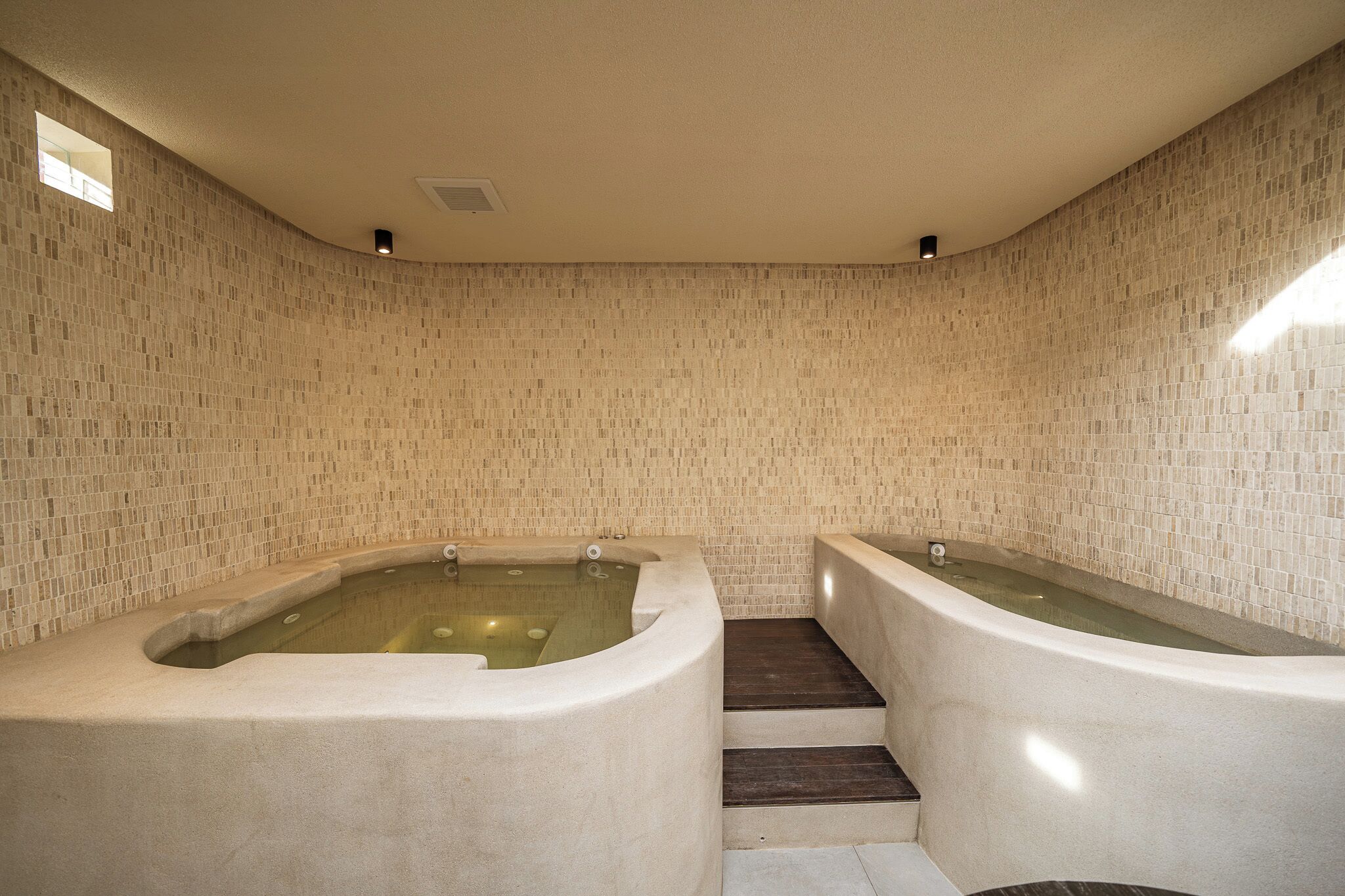 A spa room with two large tubs, a small window, and a tiled wall.