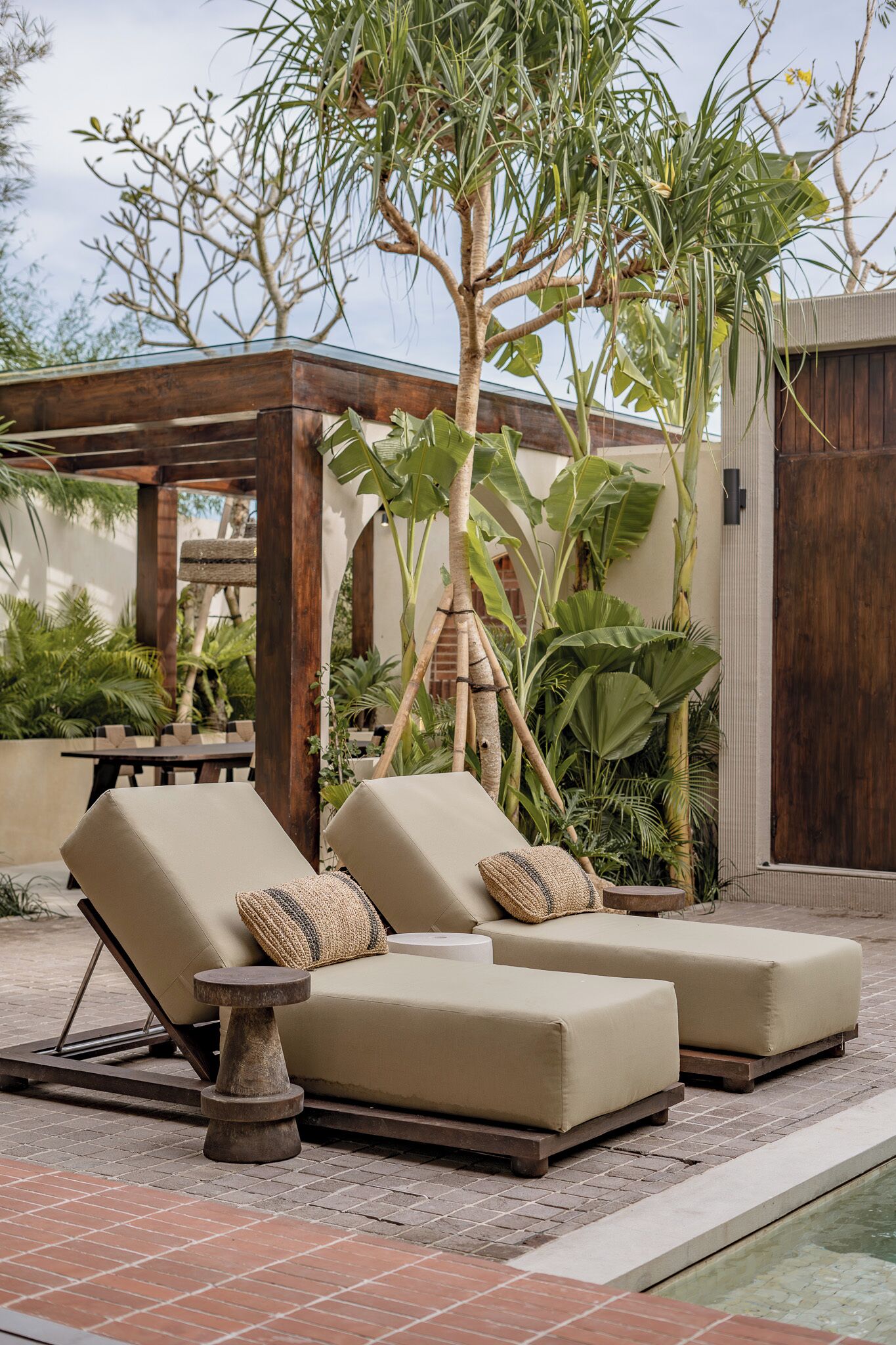 Een zwembadterras met twee beige ligstoelen, een klein rond tafeltje en een pergola.