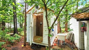A small wooden cabin with a door, surrounded by trees and a garden.