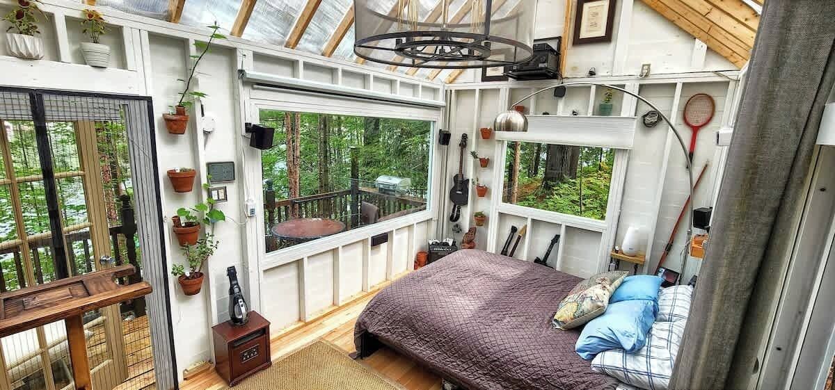 A cozy bedroom with a bed, a small table, and a window overlooking a forest.