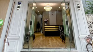 A hotel entrance with a glass door, a wooden bench inside, and a chandelier above. - Ann Apartment (Hai Phong)