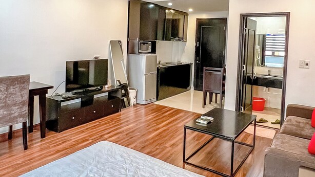A modern hotel room with a large bed, a flat-screen TV, a kitchenette, and a bathroom visible through an open door. - Ann Apartment (Hai Phong)